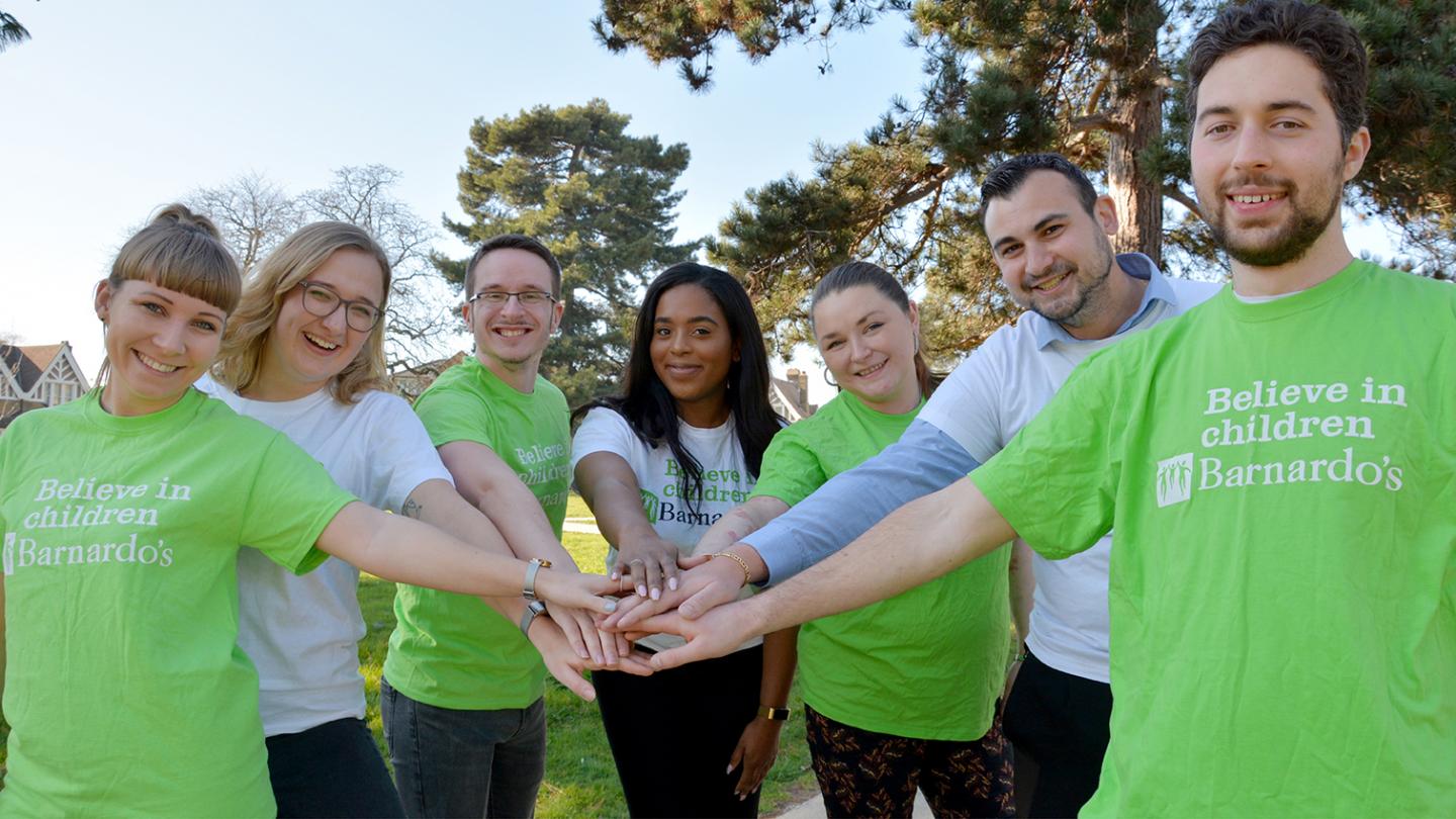 Group of Barnardo's employees reaching their hands into the centre of their group