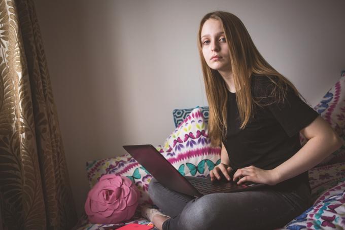 Young girl sitting on her bed looking worried holding a laptop