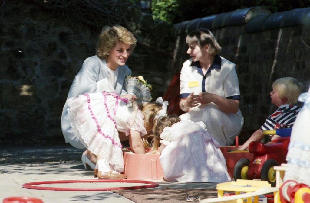 Princess Diana smiling and bending down to talk to a worker and children at a Barnardo's family centre