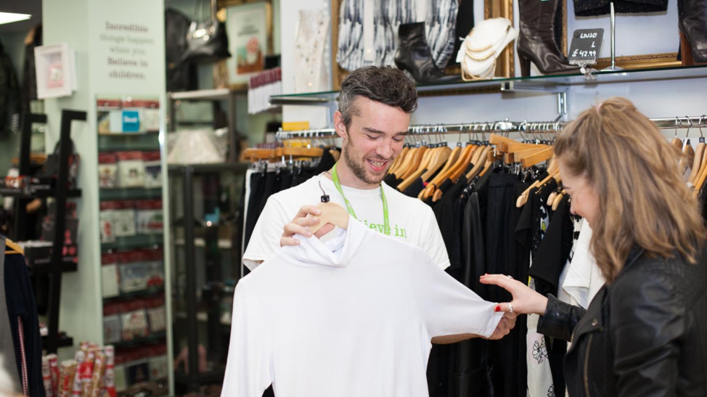 Volunteer shows a shirt to a customer in a Barnardo's charity shop