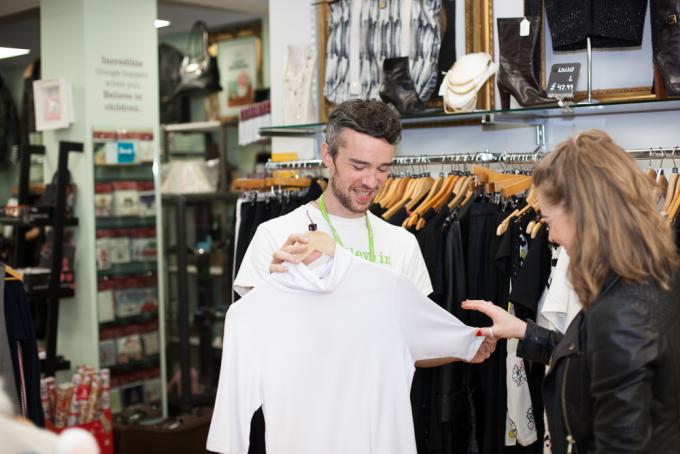 Shop volunteer holding up shirt while talking to customer