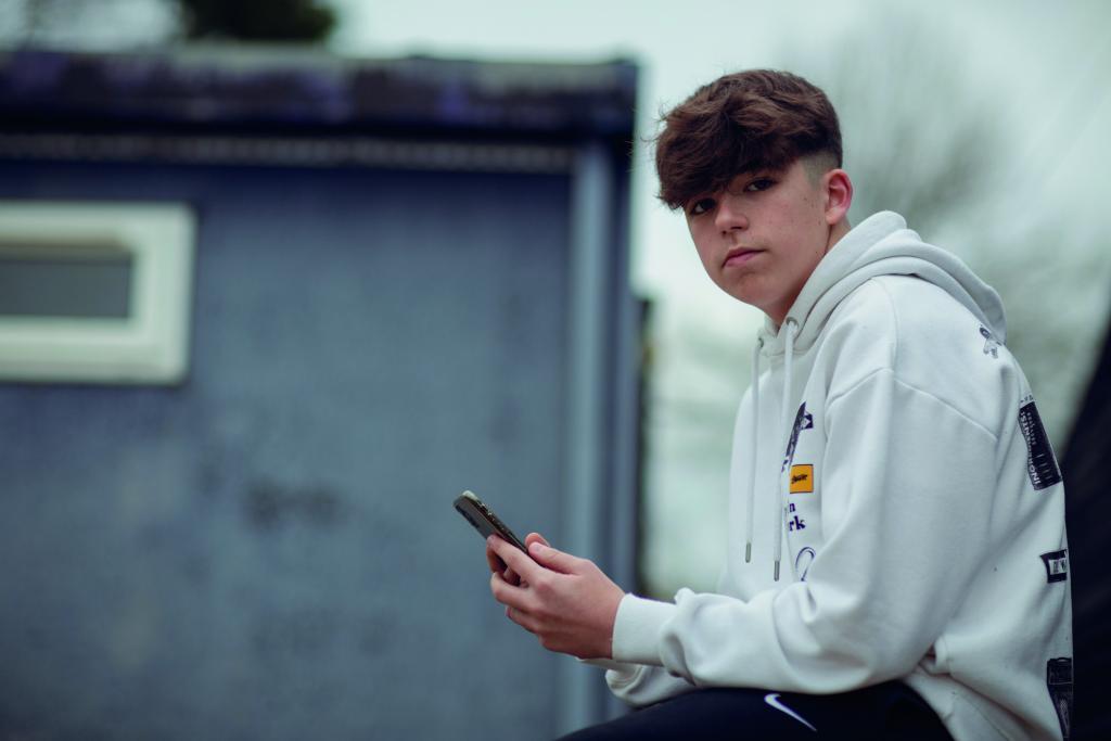A teenage boy at risk of CCE holds a mobile phone and looks at the camera