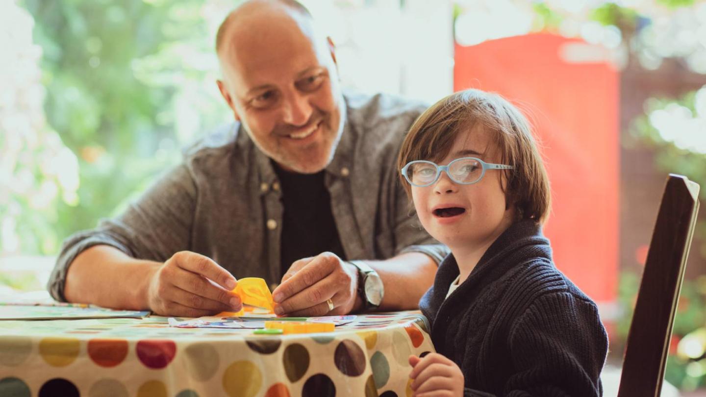 A young boy with downs syndrome sitting at a table with foster carer