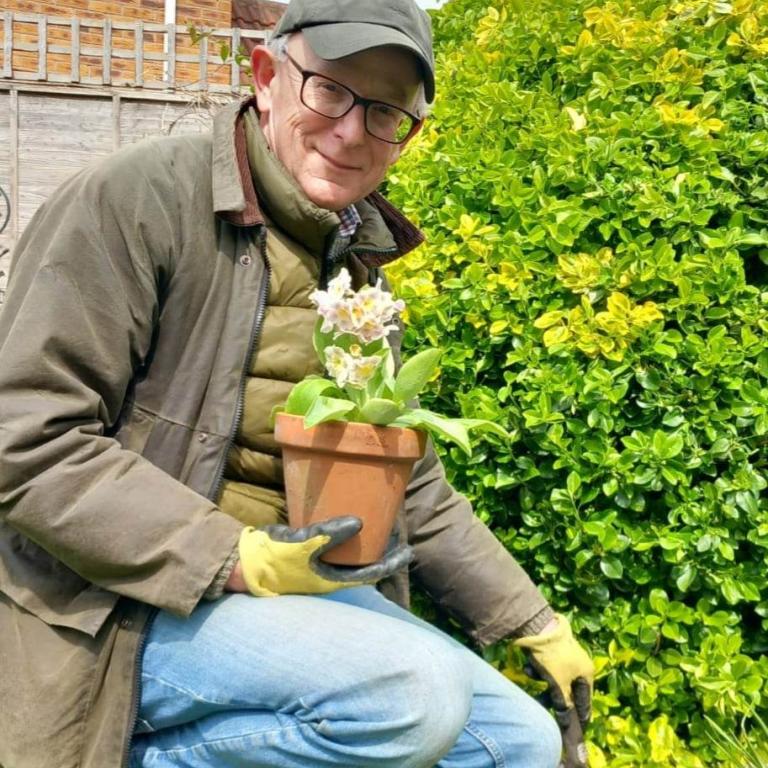 Gardening volunteer David holding a potted flower and smiling outside