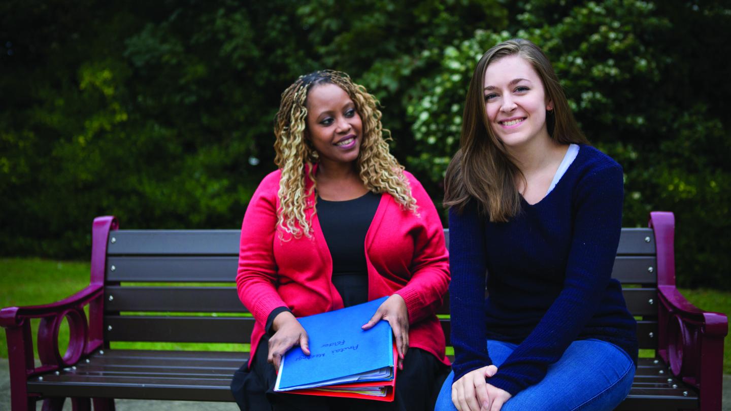 Support worker and young person sitting on park bench together.