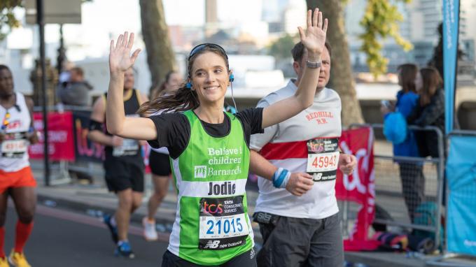 Woman running the London Marathon for Barnardo's, wearing a Barnardo's jersey, waving at the crowd