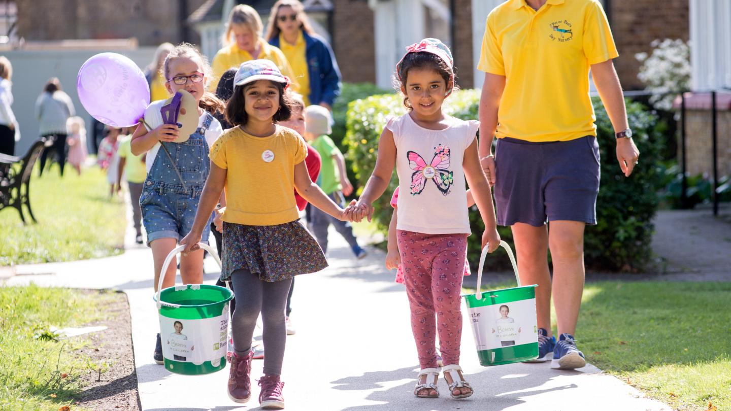 Two toddlers walking and holding hands carrying Barnardo's donation buckets