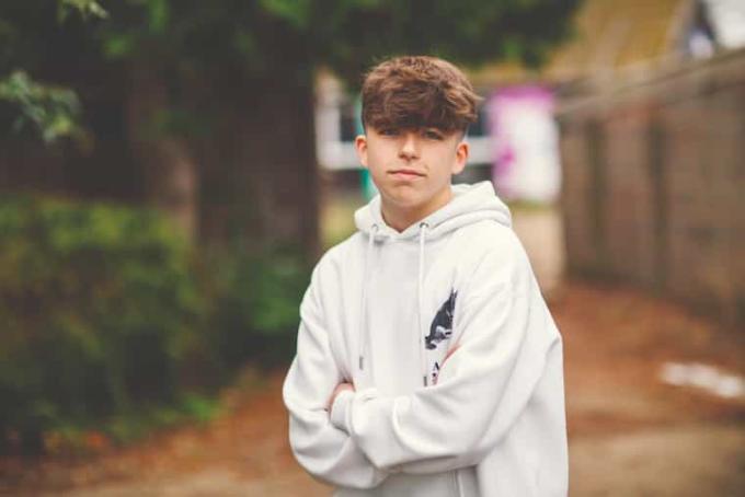 A boy in a white hoodie stands outside with his arms folded