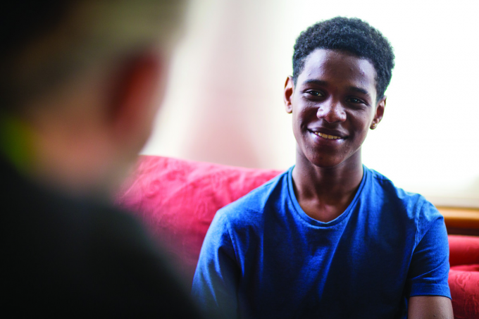 a Black boy in a blue T-shirt smiles at a barnardo's support worker in the foreground